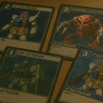 Assorted Gundam Card game War and GCG cards arranged on a wooden table.